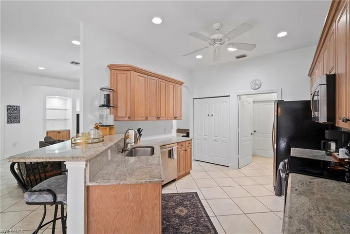 Kitchen with a breakfast bar area, light stone countertops, stainless steel appliances, sink, and ceiling fan