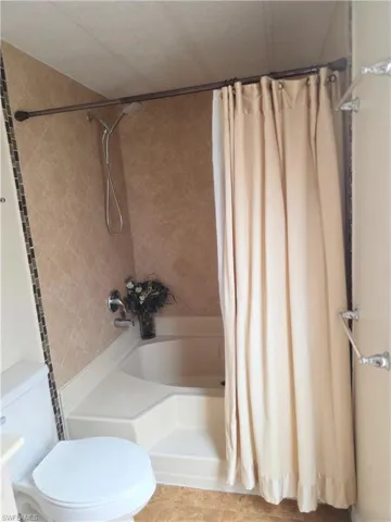 Bathroom featuring toilet and shower / bath combination with curtain