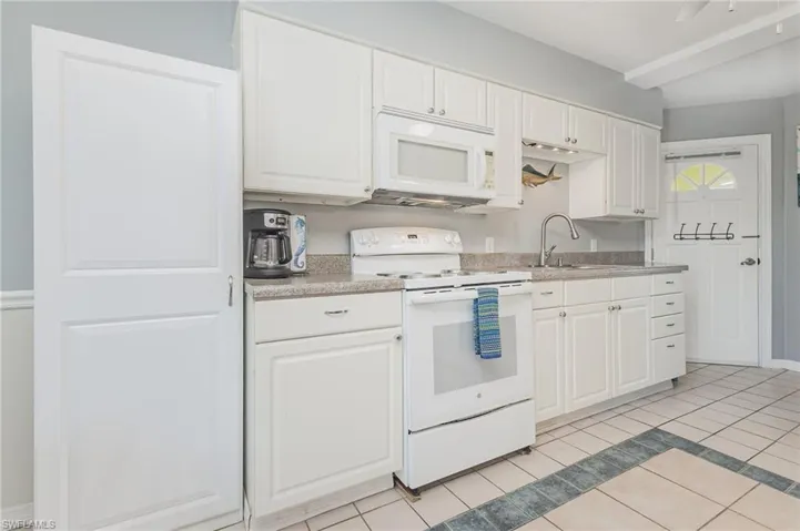 Kitchen with white appliances, white cabinetry, and light tile patterned flooring