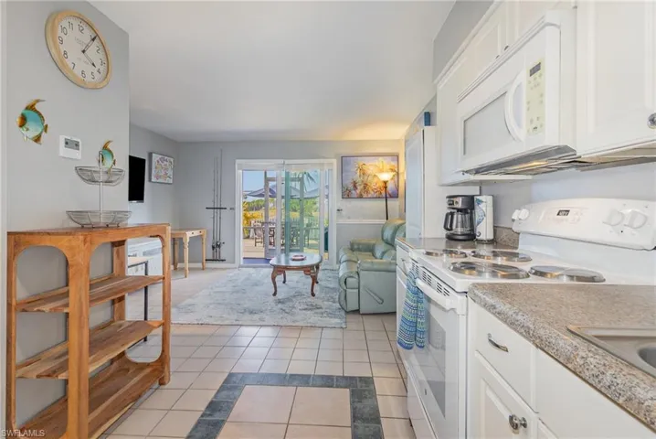 Kitchen with white appliances, white cabinets, light tile patterned flooring, and inlaid floor details