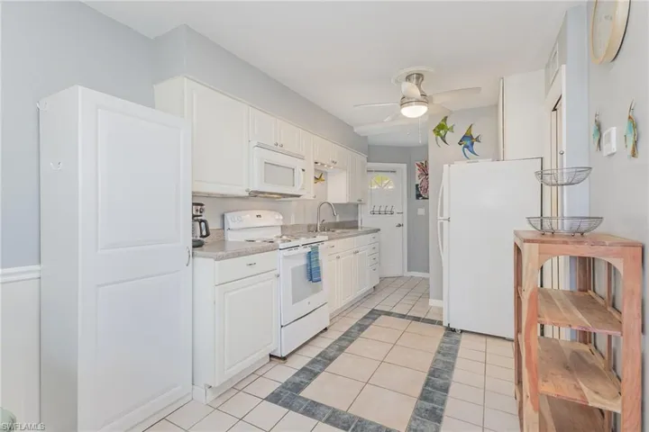Kitchen featuring white appliances, white cabinetry, inlaid floor details, light countertops, and light tile patterned flooring
