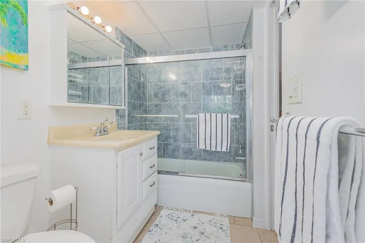 Bathroom with bath / shower combo with glass door, vanity, and light tile patterned floors