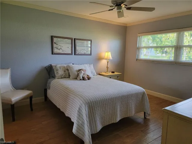 Bedroom featuring dark hardwood / wood-style flooring, ornamental molding, and ceiling fan