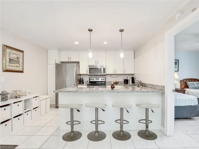 Kitchen featuring light tile flooring, kitchen peninsula, stainless steel appliances, tasteful backsplash, and white cabinets