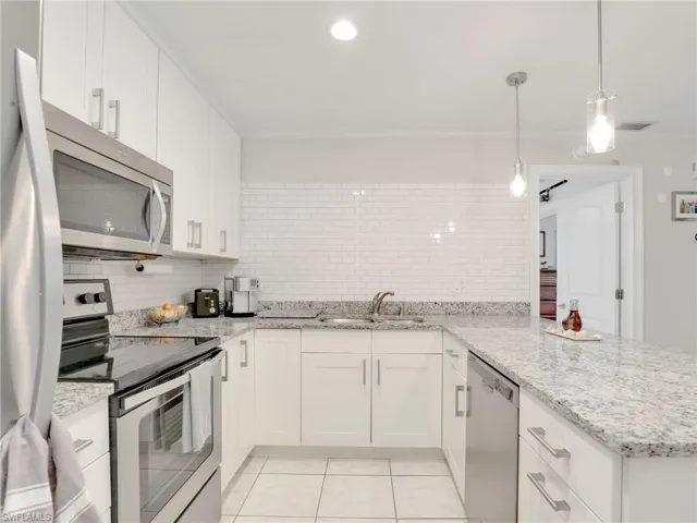 Kitchen with stainless steel appliances, white cabinets, backsplash, sink, and light tile flooring