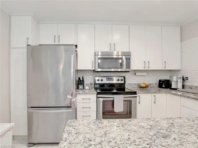 Kitchen featuring light stone counters, tasteful backsplash, white cabinetry, and appliances with stainless steel finishes