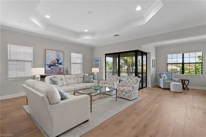 Living area with a raised ceiling, healthy amount of natural light, ornamental molding, light wood-style flooring, and recessed lighting