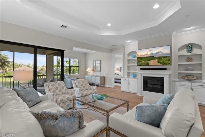 Living area with a tray ceiling, a glass covered fireplace, light wood-type flooring, recessed lighting, and crown molding