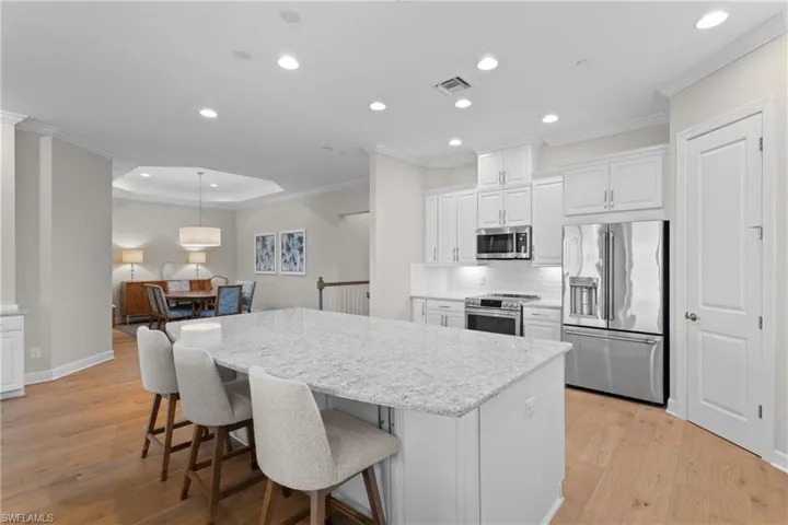 Kitchen featuring white cabinetry, ornamental molding, stainless steel appliances, open floor plan, and recessed lighting