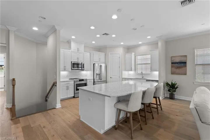 Kitchen featuring white cabinets, backsplash, light stone countertops, stainless steel appliances, and a kitchen island