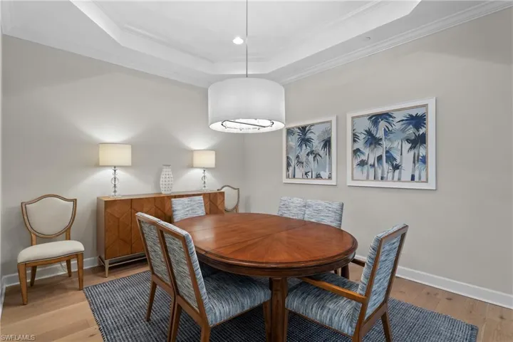 Dining space featuring ornamental molding, light wood-style floors, a raised ceiling, and recessed lighting