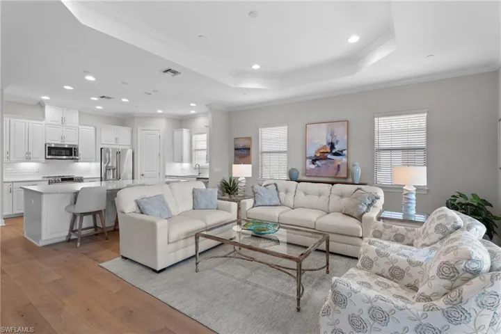 Living area with a raised ceiling, ornamental molding, recessed lighting, and light wood finished floors