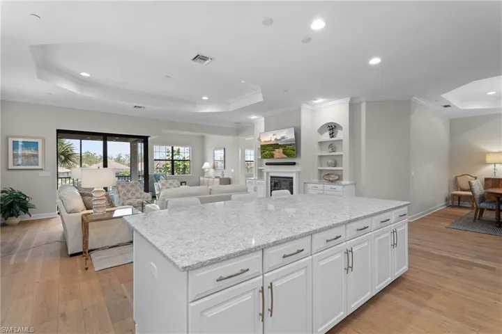 Kitchen featuring open floor plan, a tray ceiling, a glass covered fireplace, light stone countertops, and white cabinets