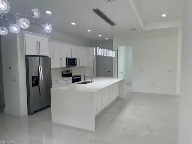 Kitchen featuring hanging light fixtures, white cabinets, appliances with stainless steel finishes, light tile patterned floors, and a kitchen island with sink