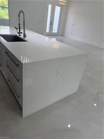 Kitchen featuring sink, tile patterned flooring, french doors, and light stone counters
