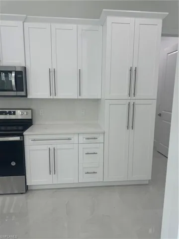 Kitchen with light tile patterned flooring, range, white cabinets, and light stone countertops