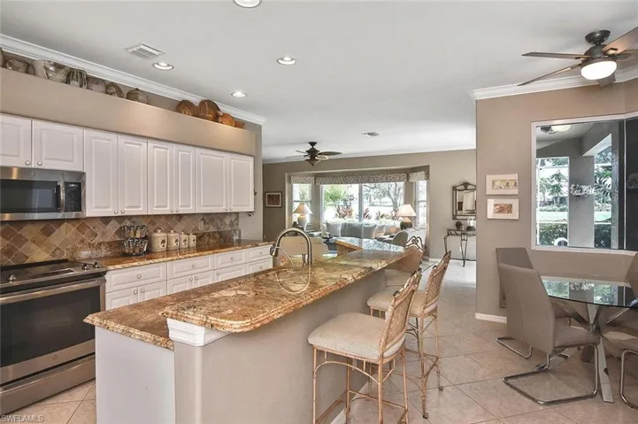 Kitchen featuring ceiling fan, crown molding, stainless steel appliances, light tile patterned floors, and tasteful backsplash