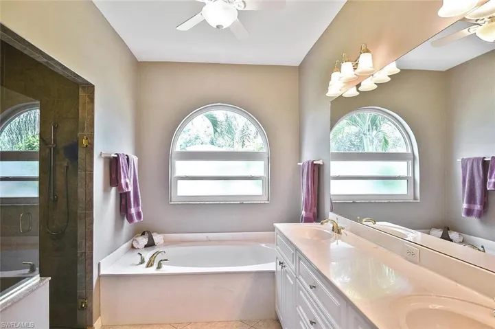 Bathroom featuring a ceiling fan, a garden tub, double vanity, and a stall shower