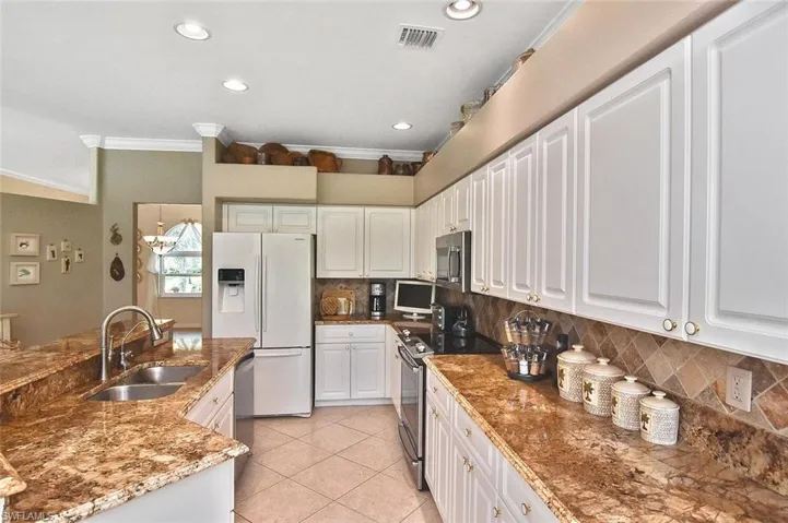 Kitchen with crown molding, appliances with stainless steel finishes, light tile patterned floors, white cabinetry, and decorative backsplash