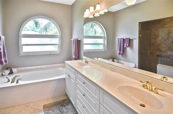 Full bath with healthy amount of natural light, a bath, double vanity, and tile patterned floors