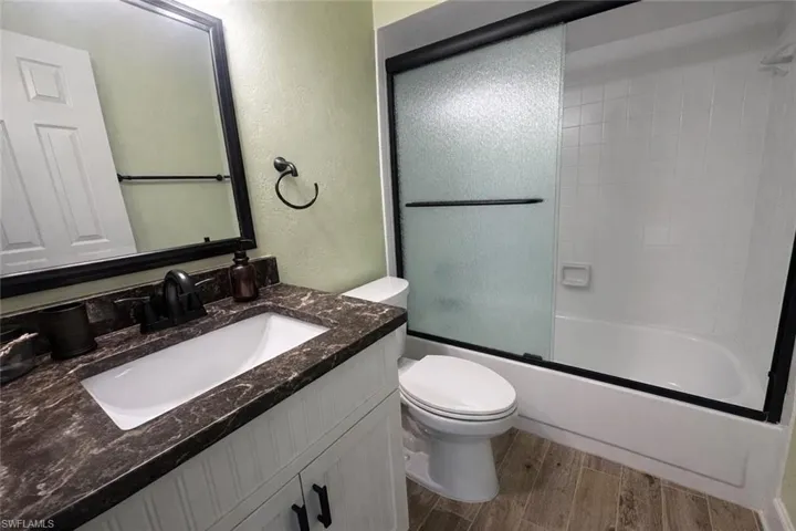 Guest Bathroom with vanity, a textured wall, combined bath / shower with glass door, and wood tiled floors