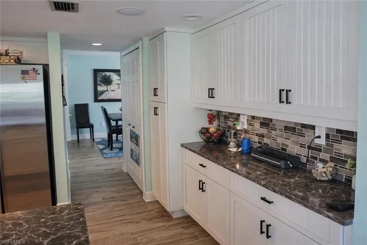 Bar area featuring freestanding refrigerator, white cabinetry, dark stone counters, light wood-type flooring, and backsplash