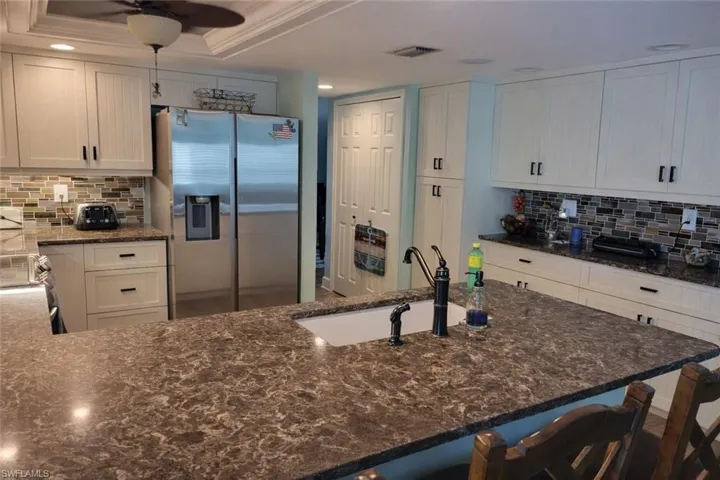 Kitchen with decorative backsplash, dark stone counters, stainless steel refrigerator with ice dispenser, and white cabinetry