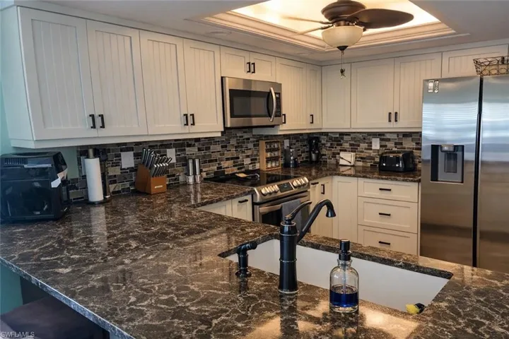 Kitchen featuring dark stone countertops, stainless steel appliances, tasteful backsplash, and white cabinets