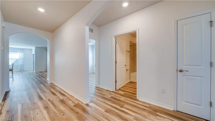 Hallway featuring arched walkways, light wood-style floors, and recessed lighting