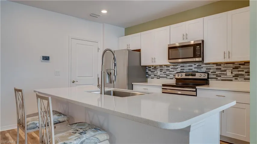 Kitchen featuring appliances with stainless steel finishes, white cabinets, light stone counters, a kitchen bar, and light wood-style flooring