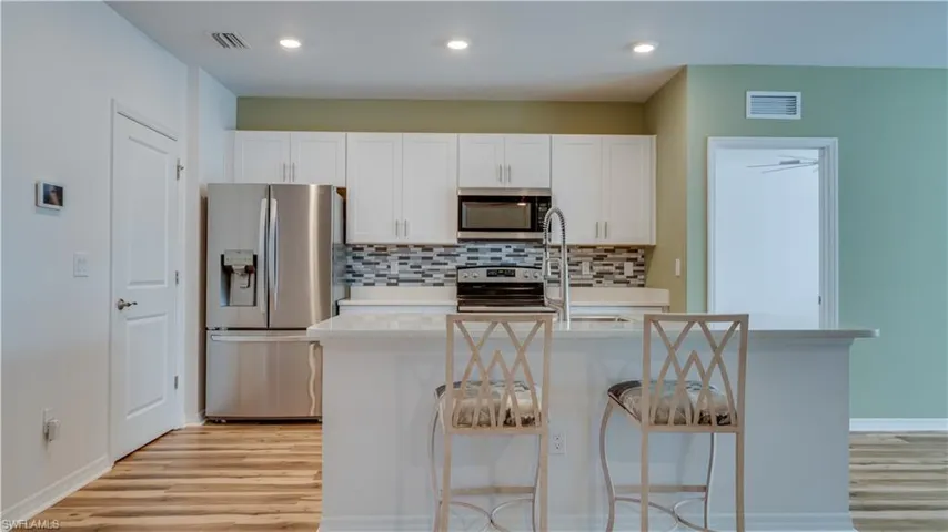 Kitchen with appliances with stainless steel finishes, white cabinetry, light stone counters, and an island with sink