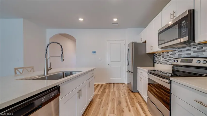 Kitchen with stainless steel appliances, white cabinets, light wood finished floors, light stone countertops, and recessed lighting
