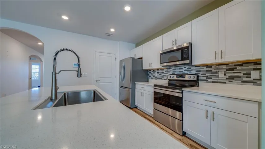 Kitchen with stainless steel appliances, white cabinets, arched walkways, light stone counters, and recessed lighting