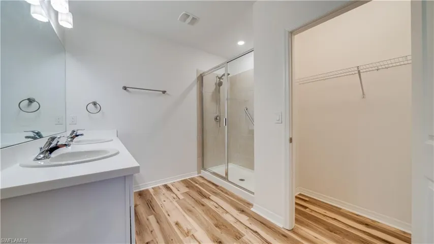 Full bath featuring double vanity, a shower stall, a walk in closet, light wood finished floors, and recessed lighting