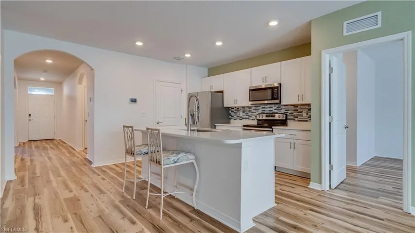 Kitchen with white cabinets, a kitchen breakfast bar, appliances with stainless steel finishes, an island with sink, and arched walkways