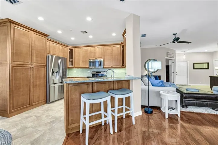 Kitchen featuring brown cabinetry, glass insert cabinets, open floor plan, a peninsula, and stainless steel appliances