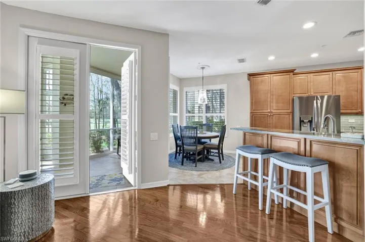 Kitchen with visible vents, brown cabinetry, stainless steel fridge with ice dispenser, a breakfast bar, and wood finished floors