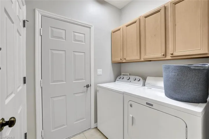 Washroom featuring light tile patterned floors, washing machine and dryer, and cabinet space