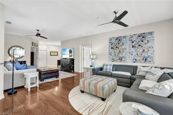 Living room with a ceiling fan, visible vents, baseboards, and wood finished floors