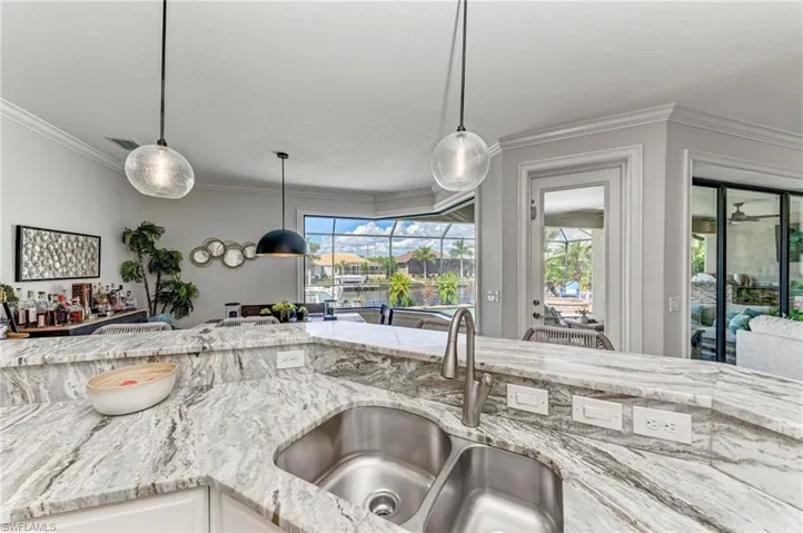 Kitchen with ornamental molding, light stone counters, a healthy amount of sunlight, and sink