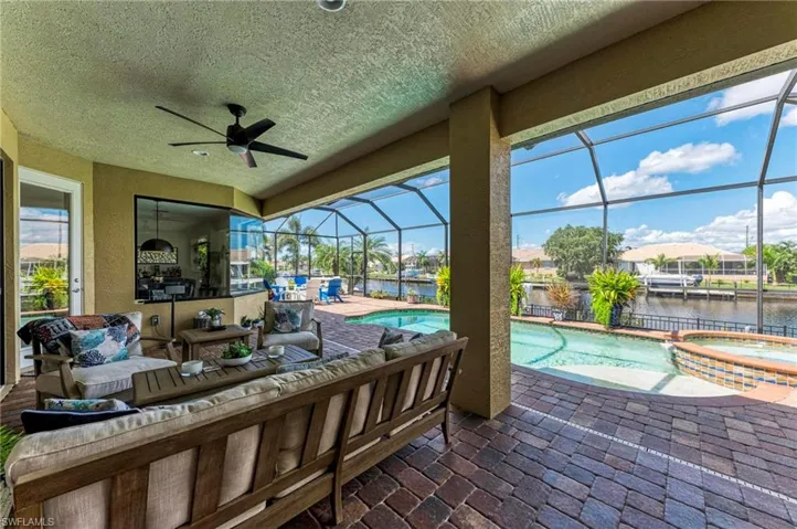 View of patio featuring a lanai, a swimming pool with hot tub, a water view, and ceiling fan