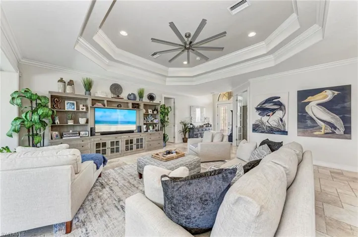 Living room featuring a raised ceiling, ceiling fan, and crown molding