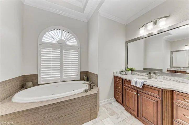 Bathroom featuring ornamental molding, vanity, and tiled tub