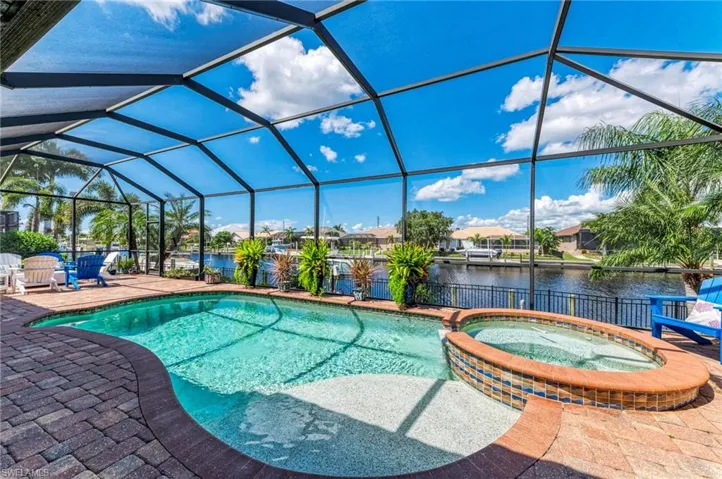 View of pool featuring a water view, glass enclosure, a patio, and an in ground hot tub