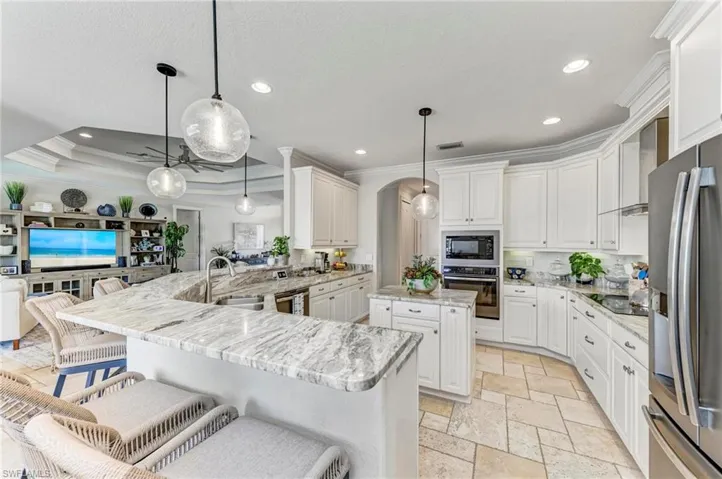 Kitchen featuring black appliances, ornamental molding, a kitchen island, hanging light fixtures, and kitchen peninsula