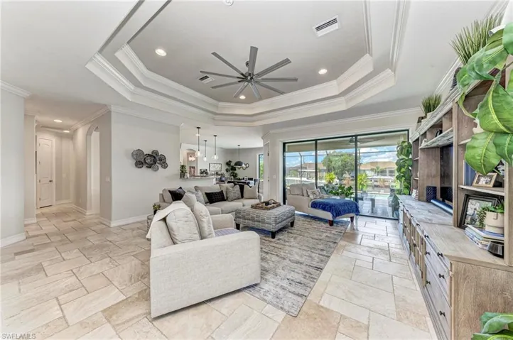 Living room with ornamental molding, ceiling fan, and a raised ceiling