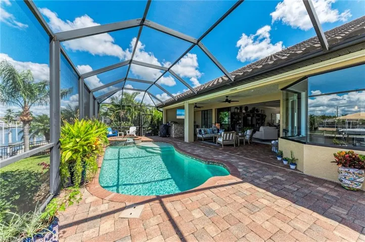 View of swimming pool with an in ground hot tub, ceiling fan, glass enclosure, and a patio area