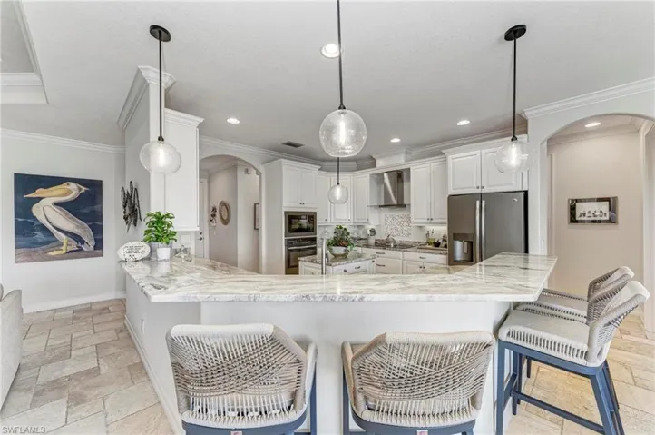 Kitchen featuring white cabinets, kitchen peninsula, ornamental molding, wall chimney range hood, and appliances with stainless steel finishes