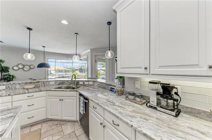Kitchen featuring white cabinets, stainless steel dishwasher, decorative light fixtures, and backsplash