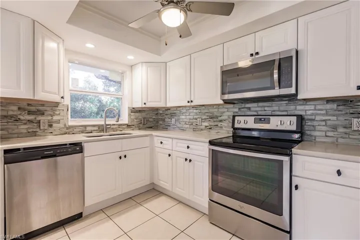 Kitchen featuring appliances with stainless steel finishes, a tray ceiling, light tile patterned floors, and white cabinets